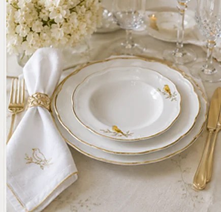 Golden Finch place setting — gold-rimmed white porcelain with finch details, embroidered napkin, and gold flatware